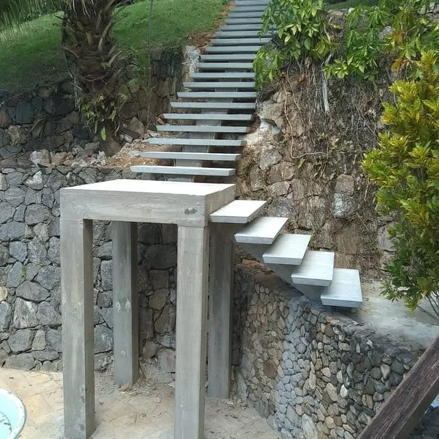 Escada externa real de concreto em execução, com patamar e degraus aparentes junto a um muro de pedras
